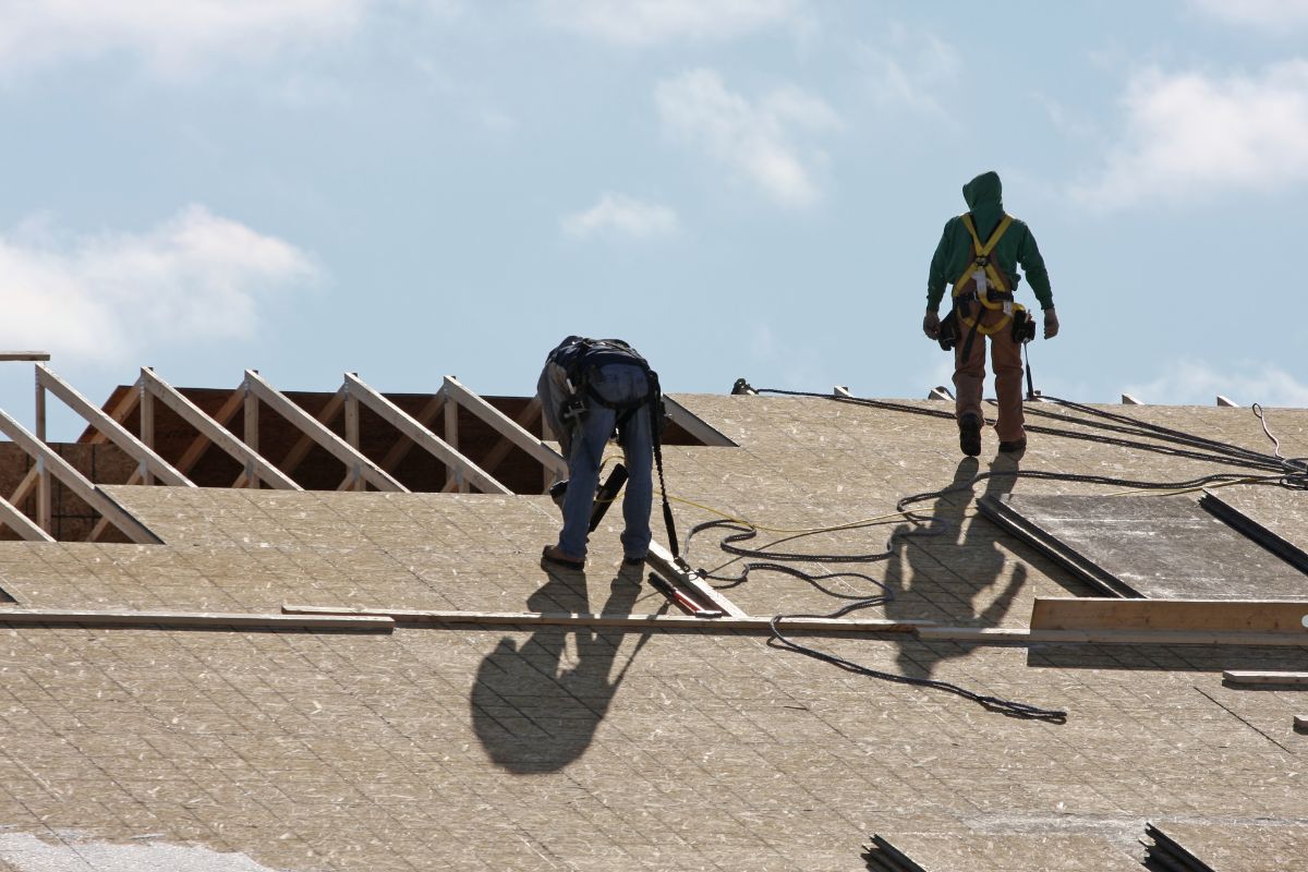 Two men sealing a roof on a house, working together to ensure proper maintenance and protection from the elements.